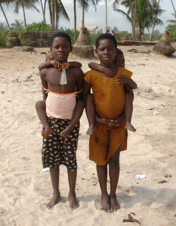 Two children giving piggyback rides on the beach at Anomabu