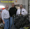 Three men examining a large diesel engine in a workshop